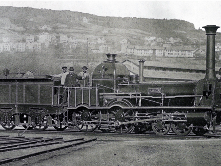 Steam locomotive Rhein of the Swiss North-East Railway (nickname: Spanisch-Brötli-Bahn) at Zurich Central Station. — © Unknown author - Barbara Graf u. a.: Bahn Saga Schweiz: 150 Jahre Schweizer Bahnen. AS Verlag, Zürich 1997, ISBN 3-905111-07-1, Seite 26, Public Domain / Wikimedia Commons